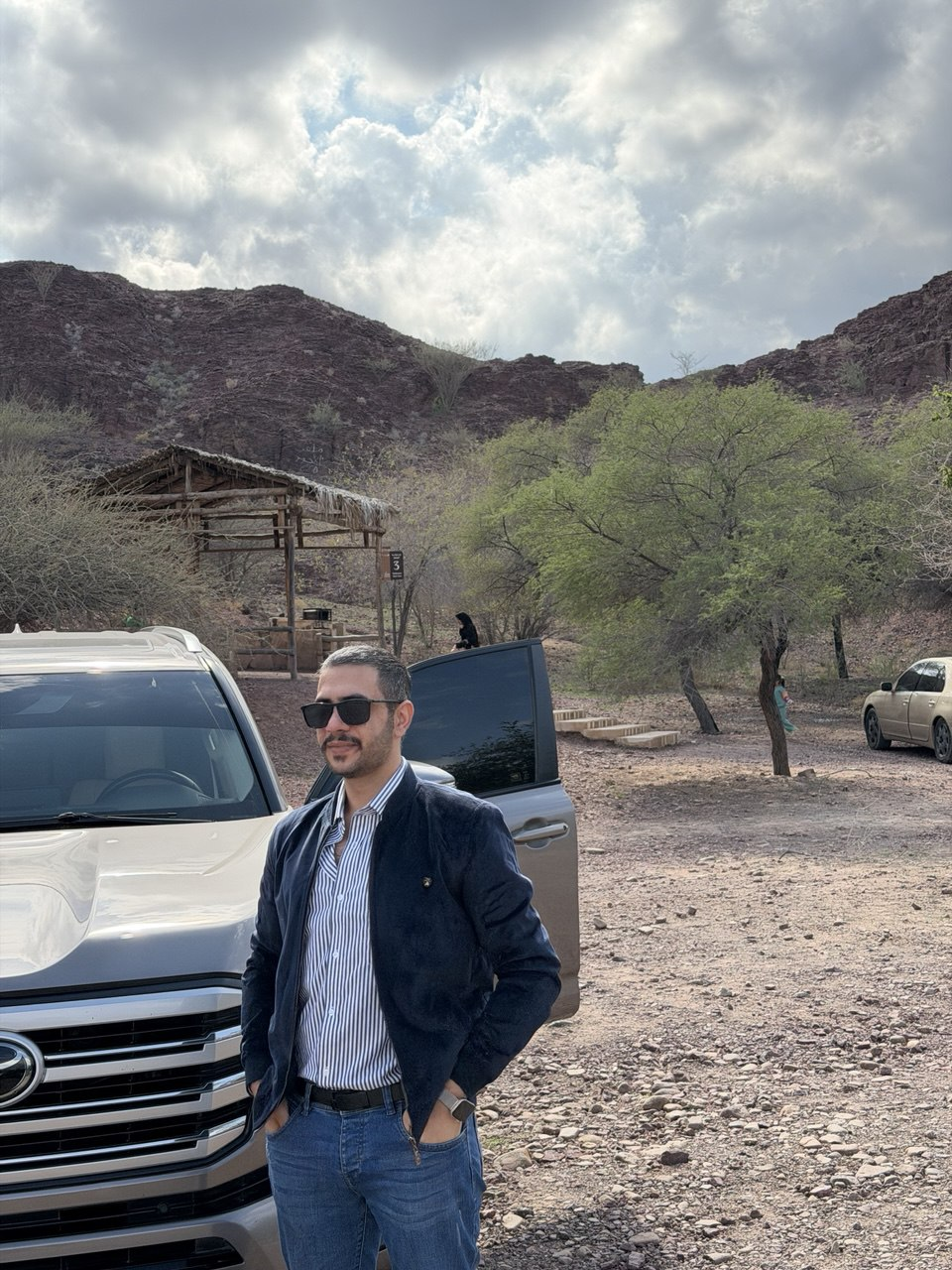 Maher outdoors beside a vehicle and mountains
